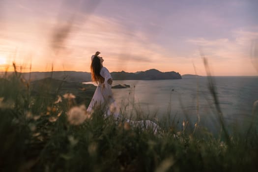 A woman stands on a grassy hill overlooking the ocean. The sky is a mix of blue and orange, creating a serene and peaceful atmosphere. The woman is enjoying the view