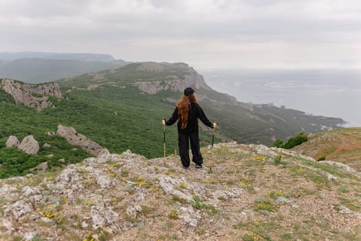 A woman stands on a mountain top, looking out over the ocean. The scene is peaceful and serene, with the woman's long hair blowing in the wind