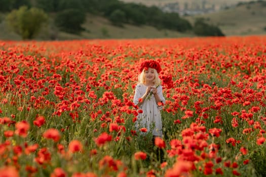 A young girl stands in a field of red poppies. She is wearing a red headband and a white dress