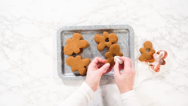 Flat lay. Gingerbread cookies, including a gingerbread man with a heart-shaped cutout, rest on a rustic metal tray against a marble countertop.