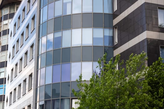 In front of the building, there is a tree, and the building itself has numerous windows. It is an urban structure, maybe a condominium or a commercial building