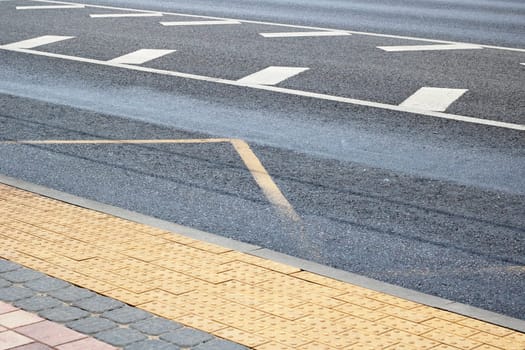 A detailed view of a road featuring a yellow curb and a white line on the asphalt surface, surrounded by grass and other landscape elements