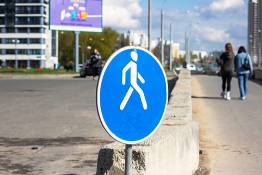 In front of a building under construction, there is a blue and white pedestrian crossing sign. The sky is visible in the background