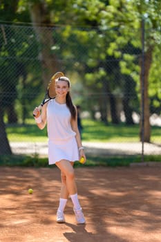 A young woman is holding a tennis racket and smiling. She is standing on a tennis court with a tennis ball in her hand
