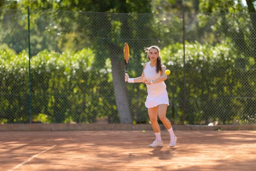 A woman is playing tennis on a court. She is wearing a white skirt and a white top