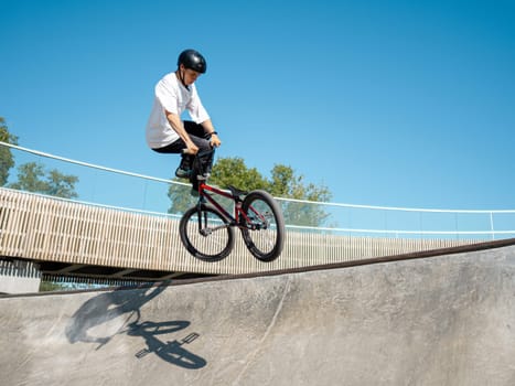 BMX bicycle rider doing stunt Tailwhip in quarter pipe. Skilled BMX freestyler athlete jumping over quarter ramp and doing aerial trick Tailwhip in street ramp park outdoors. Sunny day and blue sky