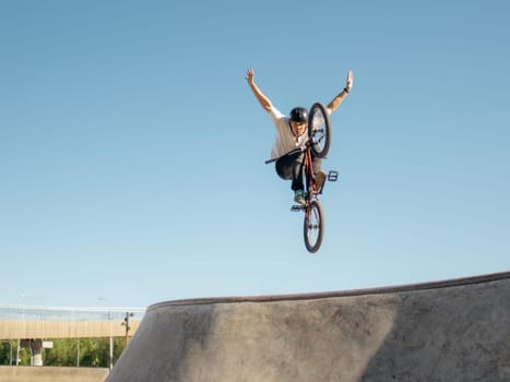 BMX bicycle rider flying and doing stunt No Hand in quarter pipe. Skilled BMX freestyler athlete jumping over quarter ramp and doing aerial trick No Hand in street ramp park outdoors