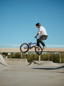 BMX bicycle rider doing stunt Bunny Hop Tailwhip. Skilled BMX freestyler athlete jumping and doing aerial trick Tailwhip Flat or Bunny Hop Tailwhip in street ramp park outdoors. Amazing blue sky