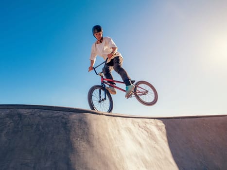 Skilled BMX rider performing Footjam trick in ramp park. Young BMX bicycle rider having fun and posing in Footjam outdoors. Footjam trick is front wheel stand. Concrete ramp street park