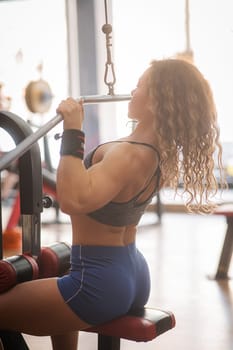 Caucasian forty-year-old woman doing lat pull-downs in the gym. Vertical photo