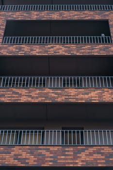 Modern European building facade, windows and balconies in row with red and brown brick decor