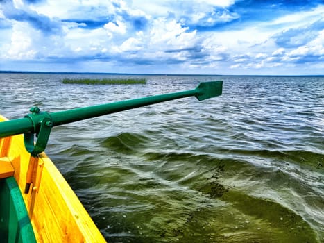 The paddle of a boat and the water of a large lake in the background. Natural landscape, travel, recreation. boat paddle extends over a calm lake