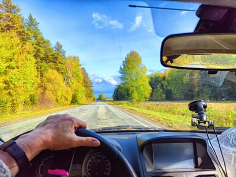 Car salon, windshield, hand on steering wheel and landscape in sunny day. View from driver on nature and Road. Single traveler. Partial focus. Blurred