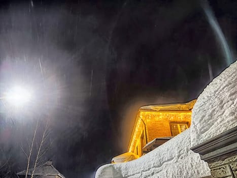 House decorated with bright Christmas garlands, surrounded by snow, under dark night sky