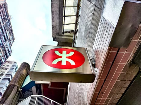 A hieroglyph meaning subway in Hong Kong on a city street. A red circle with a green symbol, the iconic sign for Hong Kongs subway system on building