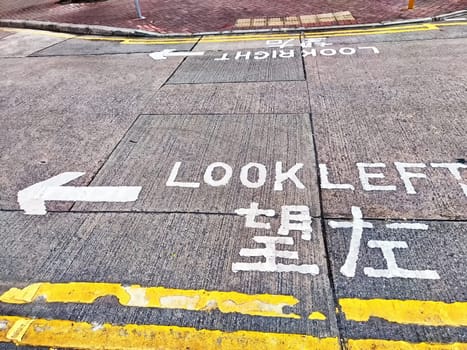 An asphalt road with a pedestrian crossing and sign instructing pedestrians to look left before crossing. Traffic safety