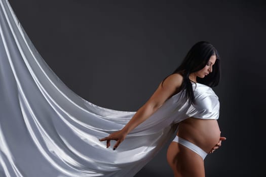 Studio photo of gorgeous pregnant woman posing with silk