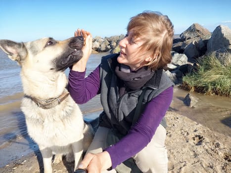 Adult girl with shepherd dog taking selfie near water of lake, river or sea. Middle aged woman and big pet on nature. Friendship, love and fun