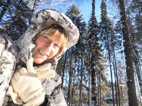 Cheerful middle aged woman in a winter warm sports jacket taking selfie on cold snow forest in nature outdoors