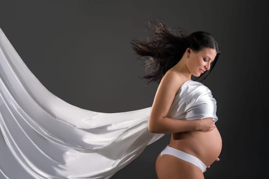 Beautiful pregnant woman poses with fluttering cloth