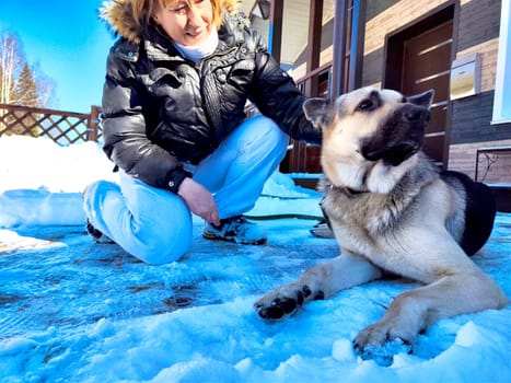 Adult girl or middle aged woman with shepherd dog near home in cold winter day with snow