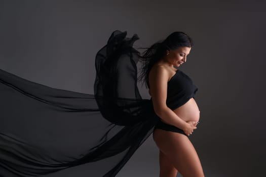 Elegant expectant mother poses with black flying cloth