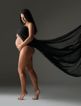 Elegant pregnant woman posing nude with flying cloth