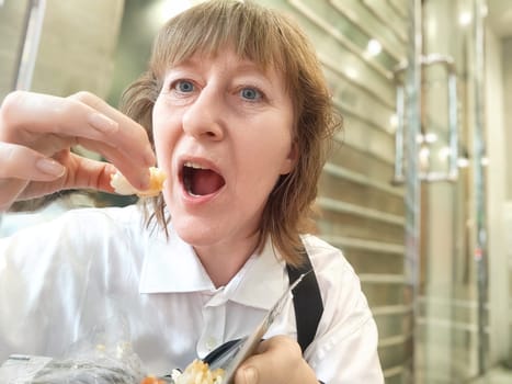 Middle-Aged Woman Enjoying Street Food on a Travel Journey in an Urban Setting, Daytime