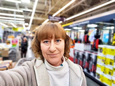 A woman smiles while taking a selfie in a brightly lit store filled with various products, including outdoor furniture.