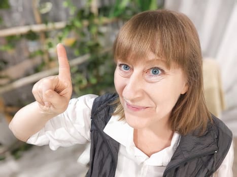 Portrait of a middle-aged woman taking selfie in a room with plants and flowers. Blogger and online streaming