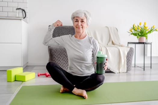 Cheerful Elderly Woman Looks Into The Camera And Shows Off Her Bicep, Embodying An Active Lifestyle And Home Workouts