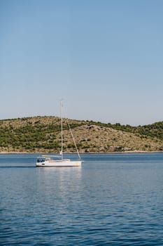 Yacht sailing along beach of Dugi Otok island under blue sky, getaway in Adriatic Sea, Croatia