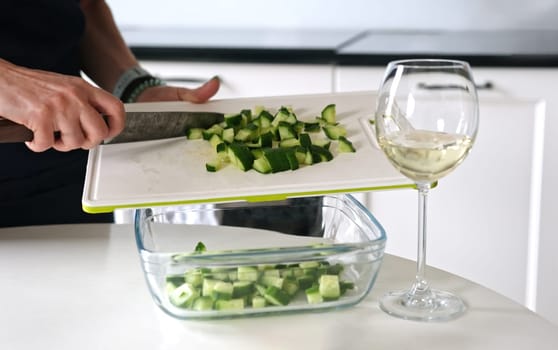 Girl Pours Chopped Cucumbers Into Bowl For Greek Salad At Home In Bright Kitchen