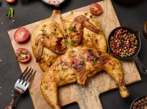 Whole fried chicken with spices on a wooden board on a black table, top view