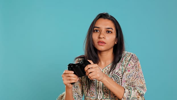 Competitive woman playing videogames with motion controlled controller, studio background. Indian Person participating in internet multiplayer racing game using gyroscope function on gamepad, camera B