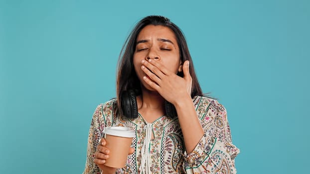 Woman suffering from insomnia yawning, sipping coffee to gain energy and get rid of pain. Tired person feeling drowsy after sleepless night, drinking caffeinated beverage, studio background, camera B