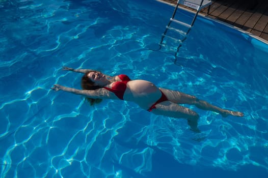 Top view of pregnant woman floating in pool in red bikini