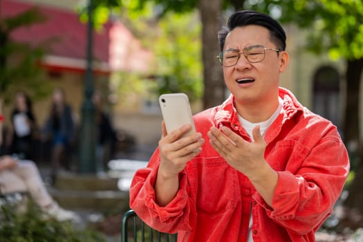 Sad Asian middle-aged man use smartphone typing browsing, fail loses lottery casino application, bad news results, fortune loss, outdoors. Chinese guy on urban city street. Town lifestyles. Horizontal