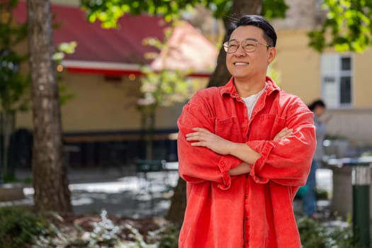 Portrait of happy Asian middle-aged man smiling friendly, glad expression looking at camera, resting, relaxation feel satisfied of good news outdoors. Chinese guy on urban city street. Town lifestyles