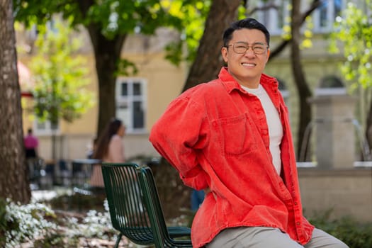 Asian middle-aged man suffering backache massaging sore place lower spine frowning from unbearable spasm torn muscles and tendons kidney stones pinched nerve outdoors. Chinese guy on urban city street