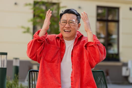 Sad unhappy Asian middle-aged man suffers from unfair situation outdoors. Problem, feeling bad, annoyed, burnout, grief. Frustrated depressed lonely mature Chinese guy standing on urban city street.