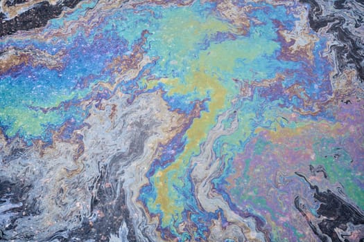 A rainbow-hued slick of spilled engine oil and gasoline spreads across the asphalt surface, creating a vibrant textured backdrop.