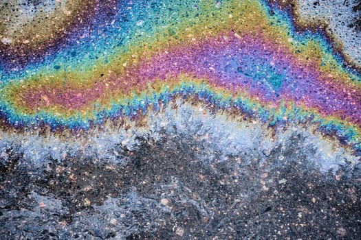 Droplets of gasoline and motor oil have accumulated on the blacktop, creating a striking abstract design through their interaction with the dark pavement