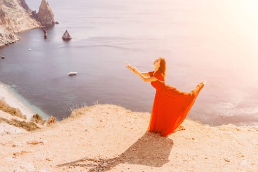 Woman red dress sea. Female dancer in a long red dress posing on a beach with rocks on sunny day. Girl on the nature on blue sky background