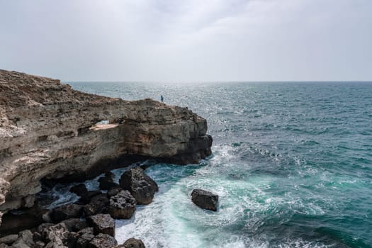 A rocky cliff overlooks the ocean, with the water crashing against the rocks. The scene is serene and peaceful, with the sound of the waves providing a calming atmosphere