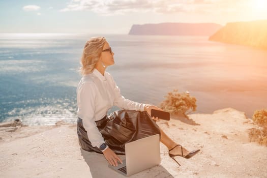 Freelance women sea. She is working on the computer. Good looking middle aged woman typing on a laptop keyboard outdoors with a beautiful sea view. The concept of remote work