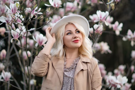 Magnolia flowers woman. A blonde woman wearing a white hat stands in front of a tree with pink flowers. She has a smile on her face and she is enjoying the beautiful scenery