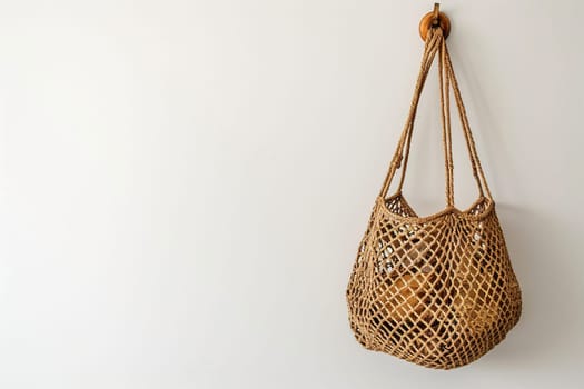 Mesh string bag hanging on a hook on a white wall with space for text.