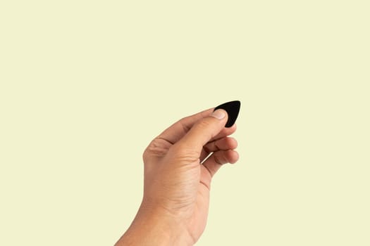 Black male hand holding a guitar pick isolated on light green background. High quality photo