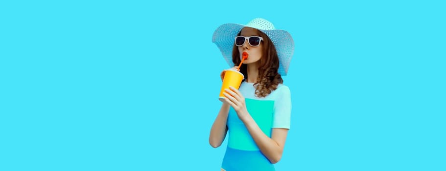 Summer portrait of beautiful caucasian young woman with cup of coffee or fresh juice wearing white straw hat on studio blue background